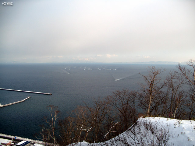 雪景色　北海道　道東 知床 羅臼（らうす） 展望台「潮風公園」から羅臼港戻る漁船を望む。　奥には国後島が見える。